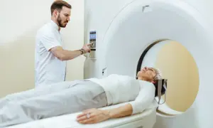 Pacjentka leży na stole do tomografii komputerowej z kontrastem. Technik obsługuje konsolę aparatu.