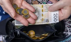 Dłonie trzymające polskie banknoty i monety nad otwartym portfelem.