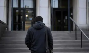 Mężczyzna w ciemnej kurtce z torbą na ramieniu wchodzi po schodach. Obok niego biegnie poręcz, która wygląda jak **list żelazny**.