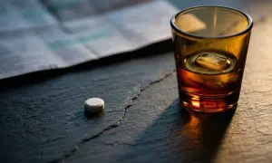 Jedna tabletka ketonalu leży obok szklanki z alkoholem i lodem. Na tle gazeta.