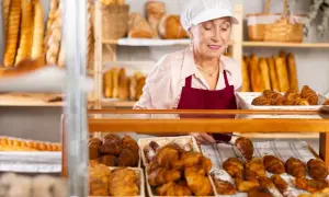 Starsza pani piekarz z uśmiechem układa świeże croissanty. To ulga dla pracujących seniorów, którzy wciąż mają pasję.