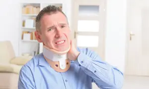 Mężczyzna w niebieskiej koszuli z widocznym bólem szyi, noszący kołnierz ortopedyczny.