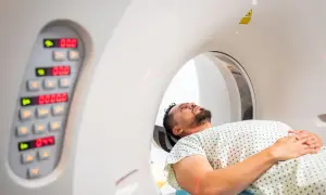 Pacjent leży w aparacie do tomografii komputerowej, przygotowując się do badania. Obok widoczny panel sterowania.