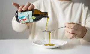 Osoba nalewa olej z butelki na łyżkę, wspierając dietę niskotłuszczową.