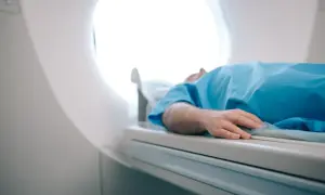 Pacjent w niebieskiej koszuli leży na stole rezonansu magnetycznego. Zastanawiasz się, ile kosztuje rezonans magnetyczny?