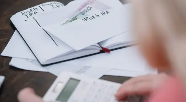 Osoba liczy pieniądze w zeszycie z wpisami "Roth IRA", zastanawiając się, czy studia liczą się do emerytury.