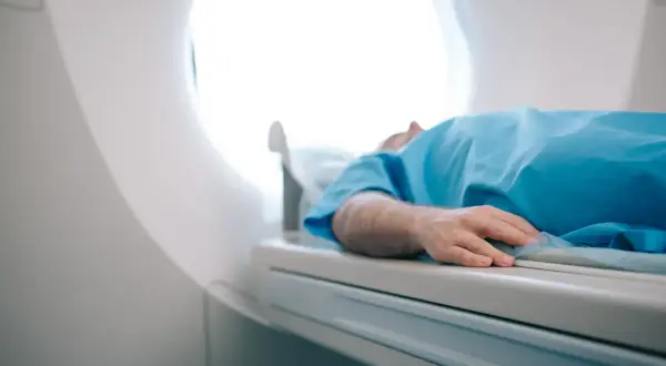 Pacjent w niebieskiej koszuli leży na stole rezonansu magnetycznego. Zastanawiasz się, ile kosztuje rezonans magnetyczny?