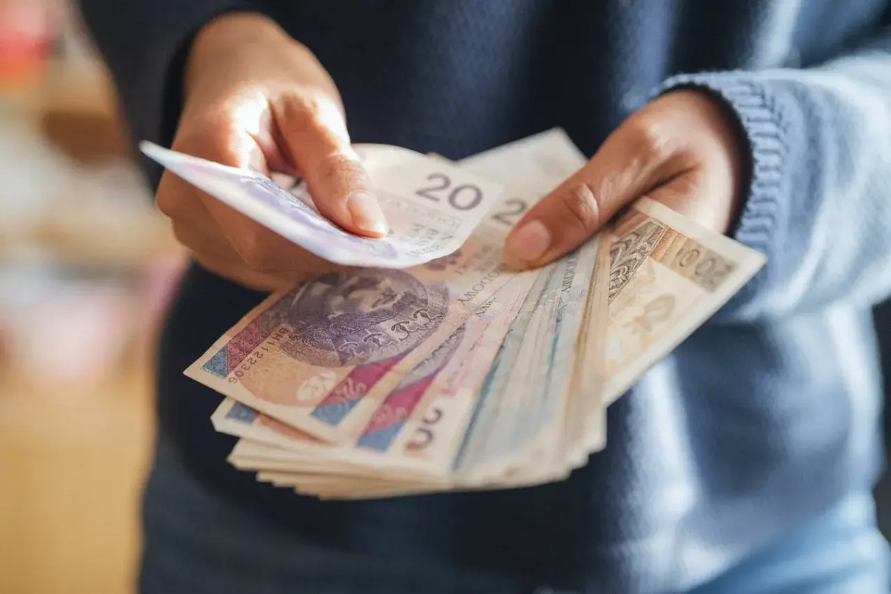 Dłonie trzymające stos polskich banknotów.