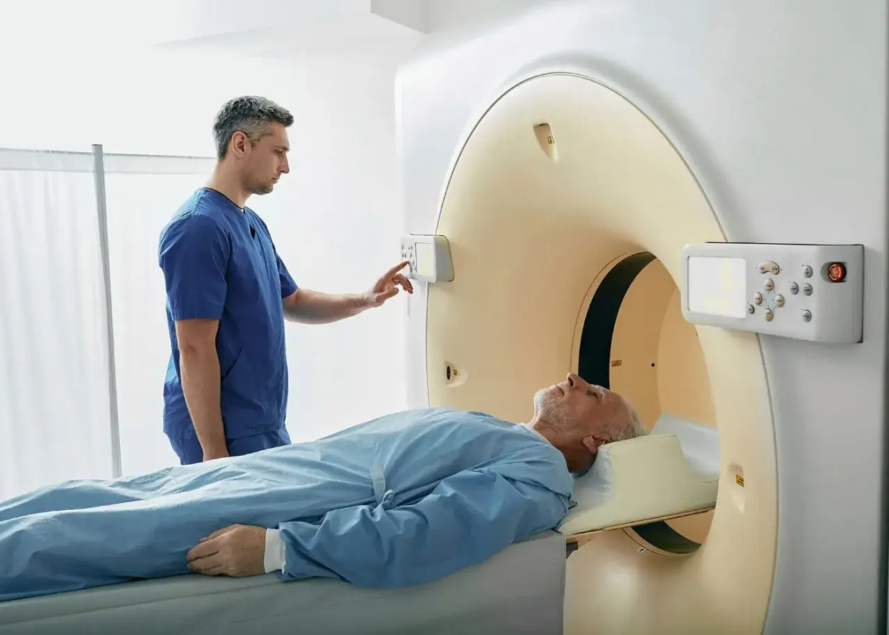 Mężczyzna leży na łóżku podczas badania tomografii komputerowej z kontrastem. Technik obsługuje panel sterowania.