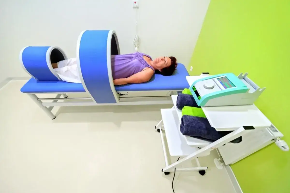 Kobieta leży na łóżku rehabilitacyjnym pod aparaturą do magnetoterapii, która może być stosowana, gdy ZUS wysyła do sanatorium na kręgosłup.