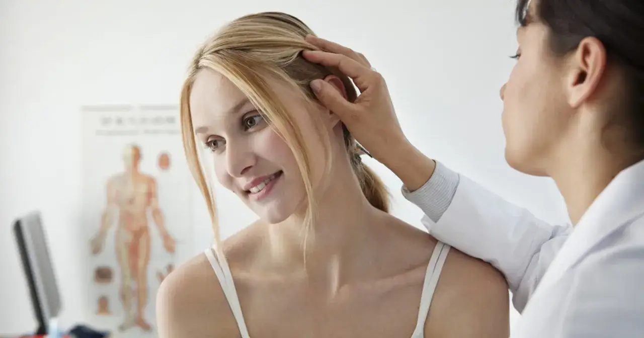 Lekarz bada skórę głowy pacjentki. Czy do dermatologa potrzebne jest skierowanie? Dowiedz się więcej.