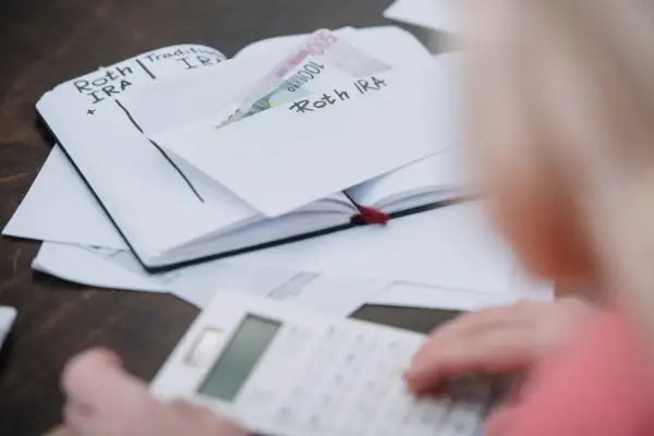 Osoba liczy pieniądze w zeszycie z wpisami "Roth IRA", zastanawiając się, czy studia liczą się do emerytury.