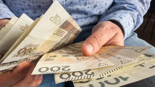 Dłoń trzyma polskie banknoty 200 zł. Finansowe przygotowania do przejścia na emeryturę.
