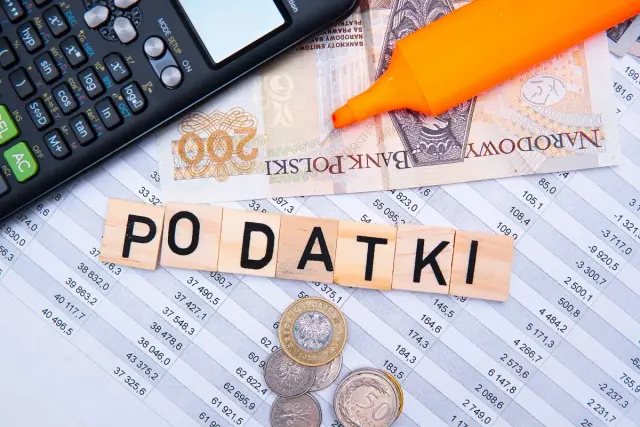 Kalkulator, banknoty i kostki z napisem "PODATKI" sugerują rozliczenia finansowe, w tym potencjalny podatek od emerytury.
